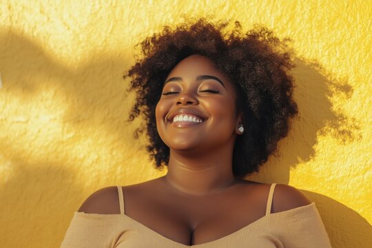 Plus size African American confident smile woman with curly black near yellow wall. Overweight black female in casual clothes in summer. photo