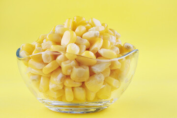 A glass cup with ripe canned corn stands on a yellow background.Canned corn grains.