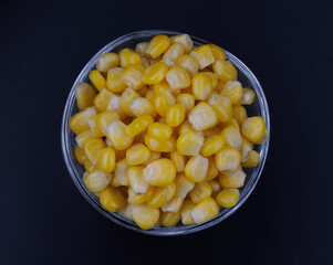 A glass cup full of canned corn grains against a black background. Canned corn grains.