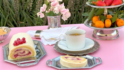 Cup positioned next to cake roll with creamy layers, berry toppings and polished silver tray highlighting refined cake presentation. Cup adds elegance to classic cake display. Vintage dessert concept.