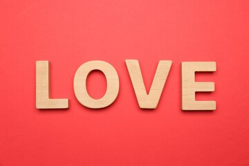 Word LOVE made of wooden letters on red background, flat lay