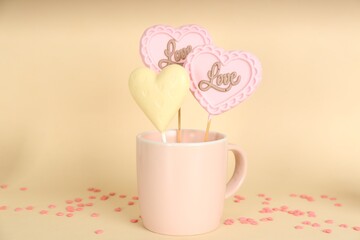 Different chocolate heart shaped lollipops in cup on beige background