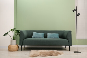 Stylish sofa with pillows, houseplant and lamp near green wall indoors