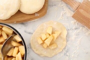 Making pirozhki (stuffed pastry pies). Pieces of dough with apples on white marble table, flat lay