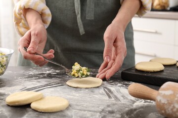 Woman making pirozhki (stuffed pastry pies) with eggs and dill at gray table indoors, closeup