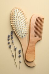 Hair brush, comb and lavender flowers on beige background, top view