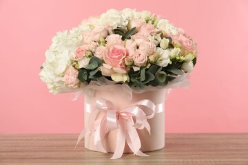 Beautiful bouquet in box on wooden table against pink background