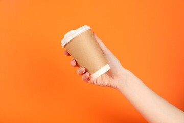 Woman holding paper cup on orange background, closeup. Mockup for design