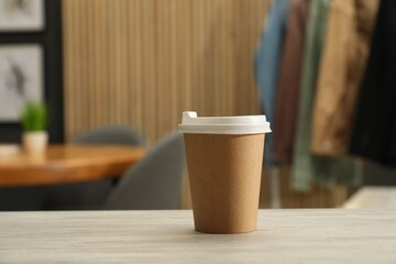 Paper cup on light wooden table indoors. Mockup for design