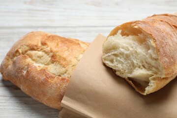 Paper bag with fresh baguettes on wooden table, closeup