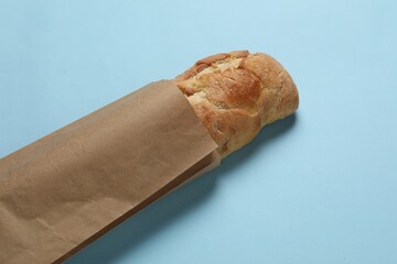 Paper bag with fresh baguette on light blue background, closeup
