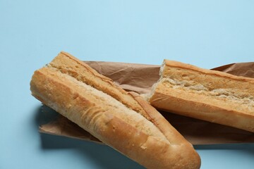 Paper bag and fresh baguette on light blue background, closeup