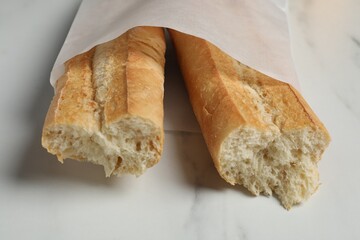 Paper bag with fresh baguette on white marble table, closeup