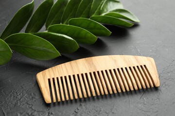 Wooden comb and branch with leaves on dark textured table, closeup