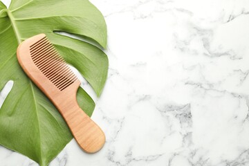 Wooden comb and monstera leaf on white marble table, top view. Space for text