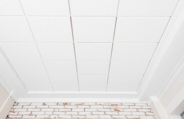 White acoustic ceiling tiles installed with white trim, brick wall. Interior design elements like molding, drywall create modern, clean look. Home renovation construction project in progress