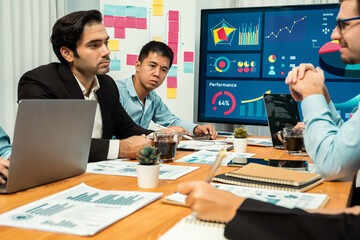 Diverse group of business analyst team analyzing financial data report. Finance data analysis chart and graph dashboard show on TV screen in meeting room for strategic marketing planning. Habiliment
