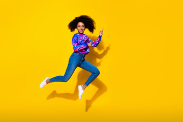 Full length photo of lovely young lady jump point empty space dressed stylish colorful blue garment isolated on yellow color background