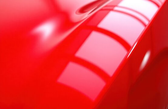 Closeup view of shiny red car paint. Glossy finish on automobile bodywork. Vivid red color with high quality reflection. Smooth surface, clean finish. New car paint details. Bright luster, texture.