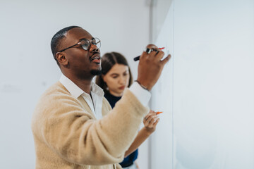 Two colleagues collaborate on a whiteboard, sharing ideas and strategies during a project...