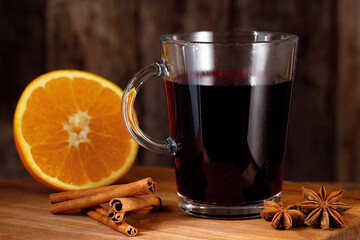 glass cup of hot mulled wine with halved orange, anise, and cinnamon sticks on rustic wooden background, aromatic warm winter drink for a cold season