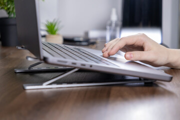 Hand typing on a laptop with an ergonomic stand in a modern workspace on a wooden desk