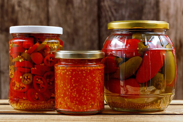 various pickled chilies in preserving jars, preserving chili peppers after harvest, sliced chilies, whole pickled jalapenos and homemade chili paste in preservation jars on a wooden background