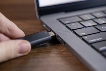 inserting usb flash drive into laptop port for data transfer and storage on wooden surface