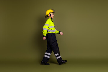 A mature female professional in vibrant protective workwear walking confidently against a khaki background