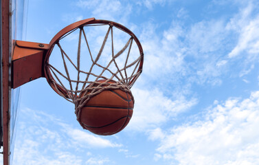 Basketball ball and basketball hoop outdoors on sky background.