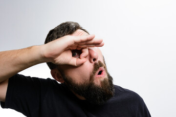 Obraz premium A man with a beard makes a surprised face while looking through a circle formed by his fingers. He wears a dark shirt against a light background.