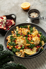 Roasted Cauliflower and roasted chickpeas salad, with pomegranate, kale, with spices, oil and lemon dressing. Vegetable winter season food on a table, vertical image.