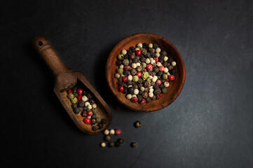 Mix of colorful peppercorns in a wooden bowl on a black background, spices.