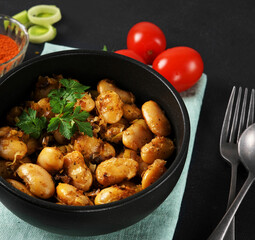 Fried beans with leeks and spices in a black bowl. close up