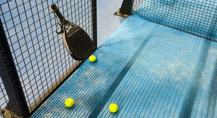 Ball in the shade of the net of a blue paddle tennis court.