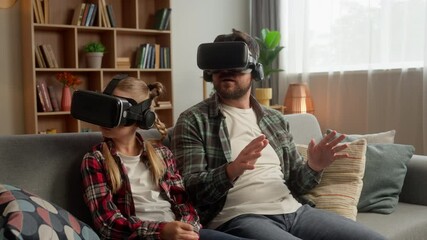 Curious Caucasian parent man dad guy male father using vr virtual reality headset glasses little schoolgirl child girl daughter kid exploring 3d world game metaverse cyberspace at home AR technology - Powered by Adobe