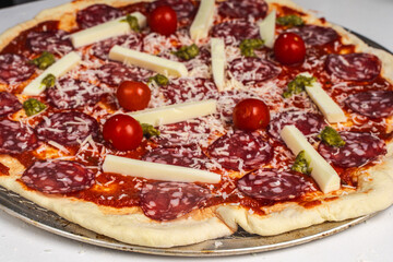 Pizza is prepared for baking. Raw pepperoni pizza with sausage, mozzarella cheese, cherry tomatoes and basil on a baking wheel