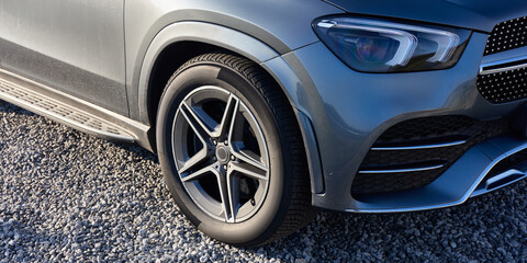 Close-up of the wheel and front headlight of a luxury silver SUV parked in a gravel parking lot.