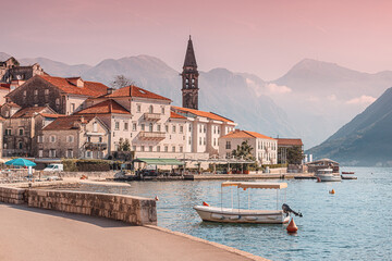 Fototapeta premium Charming waterfront scene in Perast, Montenegro, with traditional buildings, a church tower, and a small boat, all bathed in the warm light of the setting sun