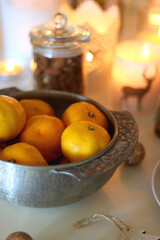 Various Christmas decorations, cookies, chocolate, nuts and tangerines, wine glasses and lit candles on the table. Holiday hygge at home. Selective focus.