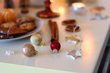 Various Christmas decorations, cookies, chocolate, nuts and tangerines, wine glasses and lit candles on the table. Holiday hygge at home. Selective focus.
