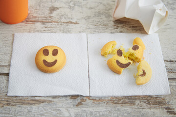 Whole smiley cookie and a disposable cup next to it on a napkin, along with a broken smiley cookie lying on a napkin next to a crumpled paper cup, spoiled mood, before and after the holidays.