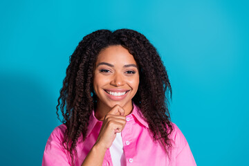 Charming young woman with curly black hair confidently smiles in a pink shirt