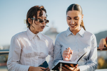 Two multiracial business women collaborating on a project while enjoying the sunset view from a...