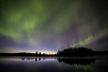 Northern lights in Kiruna, Sweden, reflecting on calm water in September with stars and forest in the background.