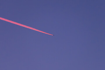 Flugzeug mit rotem Kondensstreifen am Abendhimmel
