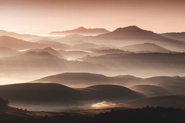 Stunning landscape of rolling hills and mountains shrouded in a golden morning mist, creating a serene and breathtaking view