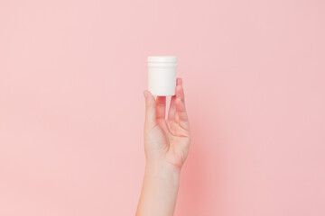 Hand holding plastic bottle on pink background. Cosmetics beauty mockup for product branding