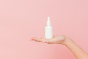 Glass cosmetic bottle for serum (hyaluronic acid and collagen) in hand on pink background. Beauty concept