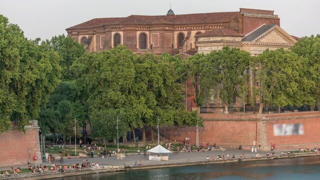 Aerial view of Port de la Daurade park along the Garonne River timelapse in Toulouse, France. Sunset orange light, ferry at the dock and people enjoying the vibrant riverside atmosphere